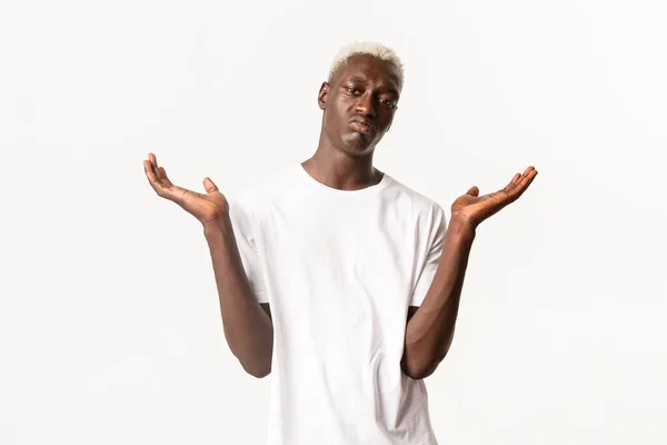 Portret van onverschillig Afrikaans-Amerikaanse blonde man, shrugging en verspreid handen zijwaarts clueless, staande witte achtergrond — Stockfoto