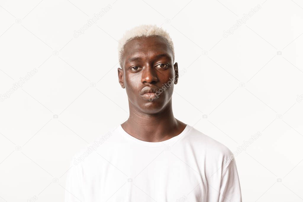 Close-up of serious handsome african-american blond stylish guy, looking at camera determined and calm, standing white background