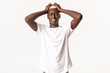 Endişeli Afro-Amerikalı sarışın adamın portresi, el ele tutuşup yüzünü buruşturan, bela yüzünden panikleyen, beyaz arka planda duran