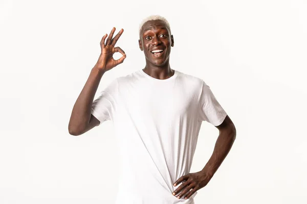 Πορτρέτο του διασκεδασμένου αφροαμερικανού, δείχνει εντάξει χειρονομία σε έγκριση, όπως κάτι ή να συστήσει, στέκεται λευκό φόντο — Φωτογραφία Αρχείου