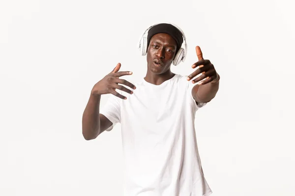 Portret van vrolijke coole Afrikaans-Amerikaanse man, dansen en luisteren muziek in hoofdtelefoon, witte achtergrond — Stockfoto
