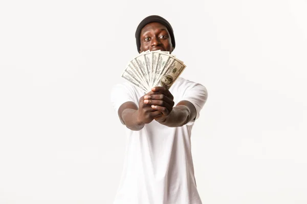 Portrait of cheerful african-american guy giving you money or show cash, standing white background — Stok Foto
