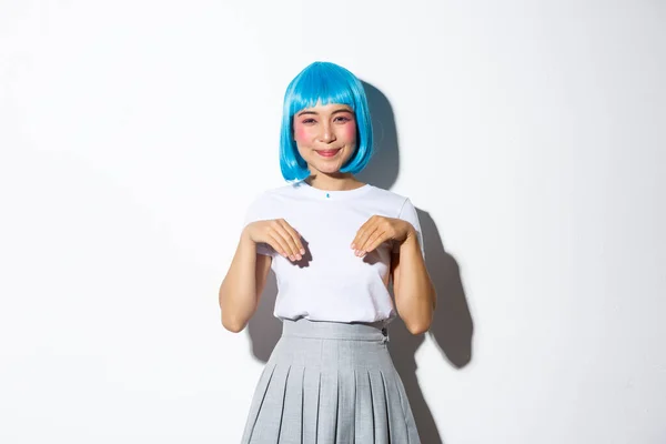 Портрет милой улыбающейся азиатской девушки в голубом парике и костюме школьницы, играющей вокруг и действующей как котенок, стоящей на белом фоне — стоковое фото