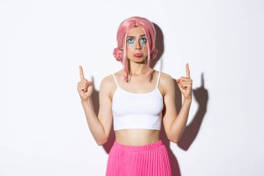 Pembe peruklu zavallı parti kızı portresi, hıçkıra hıçkıra ağlıyor ve somurtuyor, hayal kırıklığına uğramış görünüyor ve parmaklarını kaldırıp beyaz arka planda duruyor.