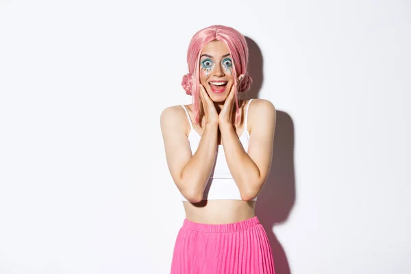 Obraz podekscytowany strony dziewczyna w różowej peruce i jasny makijaż patrząc pod wrażeniem, uśmiechnięty i patrząc zaskoczony, stojąc na białym tle — Zdjęcie stockowe