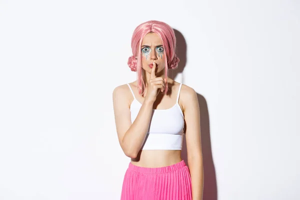 Imagem de menina carrancuda com raiva em peruca rosa e maquiagem halloween, shushing para alguém, repreendendo pessoa por ser muito alto, de pé sobre fundo branco — Fotografia de Stock