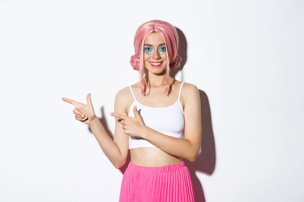Gambar gadis trendi yang tersenyum berpakaian untuk pesta halloween, menunjuk jari kiri, menunjukkan iklan, berdiri di atas latar belakang putih — Stok Foto