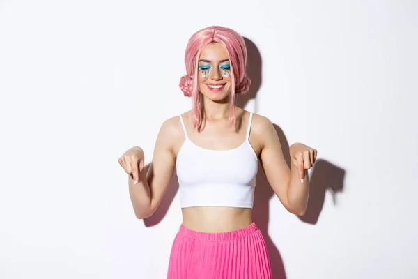 Feliz mulher sorridente vestida para festa de Halloween, celebrando férias e peruca rosa e maquiagem brilhante, apontando os dedos para o seu logotipo — Fotografia de Stock