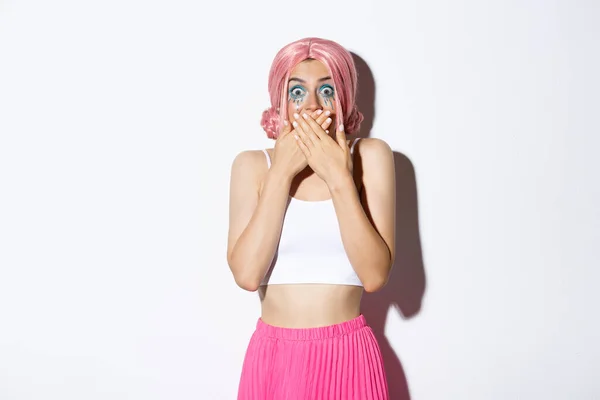 Image of girl smiling and laughing, cover mouth with hands and looking at camera amused, standing in pink wig and bright outfit for halloween party