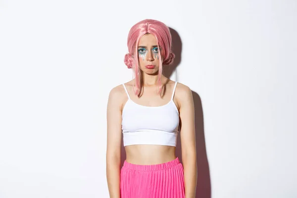 Πορτρέτο του λυπημένος χαριτωμένο κορίτσι με Απόκριες μακιγιάζ και ροζ περούκα αναζητούν αναστατωμένος, κατσούφιασμα και διαμαρτύρονται για κάτι, στέκεται πάνω από το λευκό φόντο — Φωτογραφία Αρχείου
