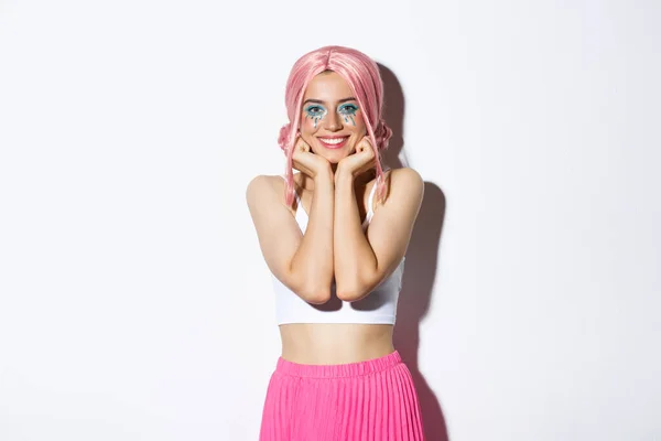 Νεαρό υπέροχο κορίτσι κόμμα με ροζ με και αποκριάτικο μακιγιάζ κοιτάζοντας κάτι με θαυμασμό και ενδιαφέρον, χαμογελώντας ανόητο, στέκεται πάνω από το λευκό φόντο — Φωτογραφία Αρχείου