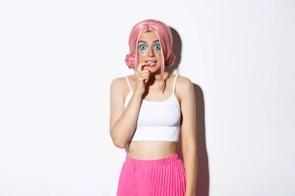 Image of timid cute girl in pink wig, looking indecisive and biting finger, standing over white background — Stock Photo, Image