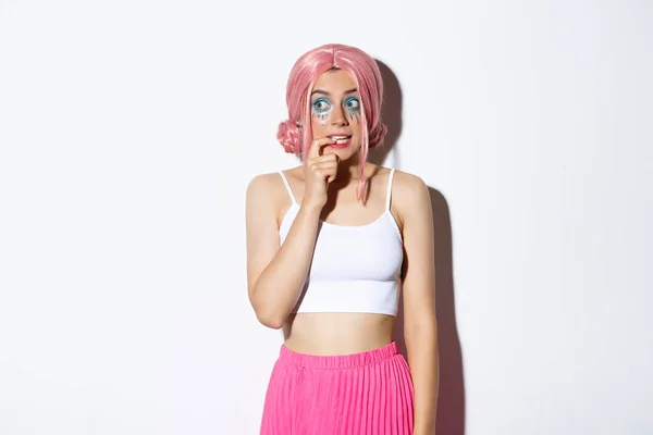 Obraz głupie piękne dziewczyny z różową peruką i makijaż halloween, gryzienie palec i patrząc kuszony w lewo, chcą coś, stojąc nad białym tle — Zdjęcie stockowe