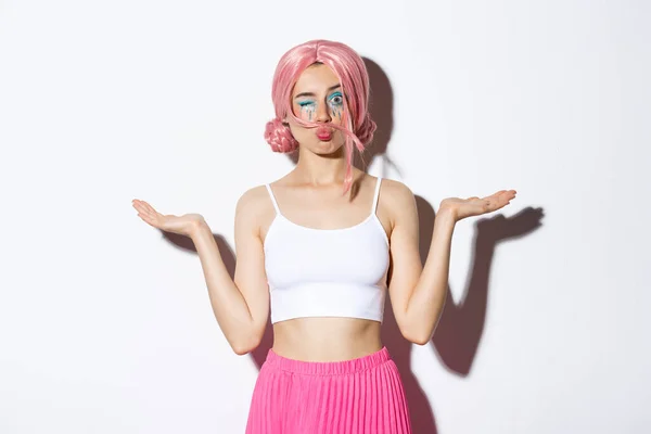 Portret głupiej pop dziewczyny w różowej peruce, mrugającej do kamery trzymającej coś w obu rękach, stojącej nad białym tłem — Zdjęcie stockowe