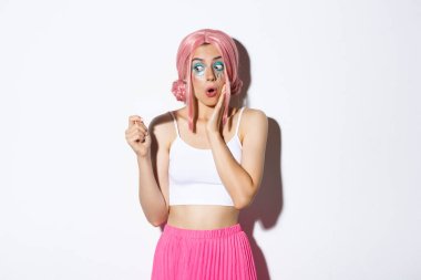 Pembe anime peruklu ve parlak makyajlı heyecanlı aptal bir kız görüntüsü. Kredi kartına, tatil alışverişine, beyaz arka planda dikilmeye hayran bakıyor.