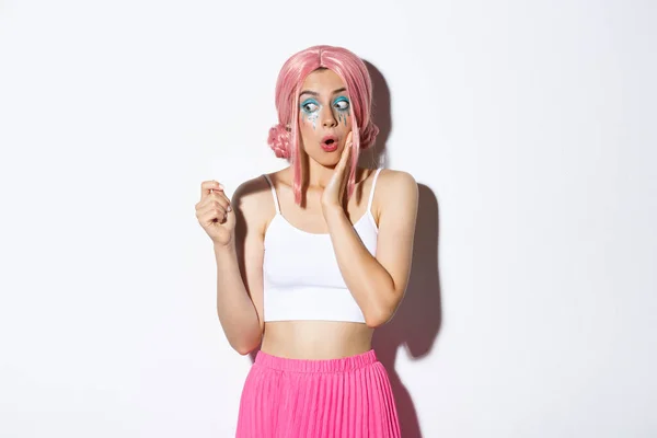Obraz podekscytowany głupią dziewczyną w różowej peruce anime i jasny makijaż, patrząc zdumiony karty kredytowej, zakupy na wakacje, stojąc nad białym tle — Zdjęcie stockowe
