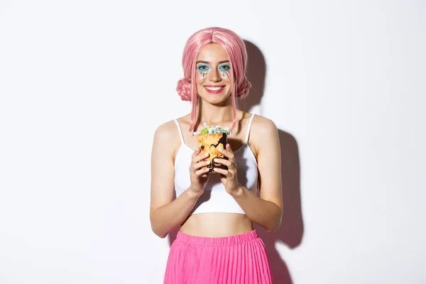 Imagem da bela menina sorridente em rosa peruca segurando truque ou doces, celebrando o dia das bruxas, de pé sobre fundo branco — Fotografia de Stock