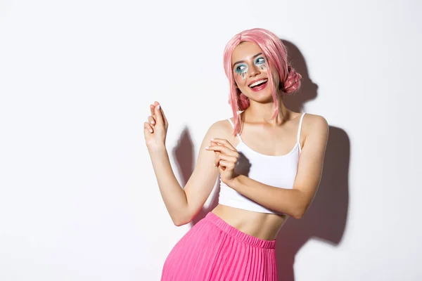Imagem de menina festa atraente com peruca rosa e maquiagem brilhante, se divertindo e comemorando férias, dançando feliz sobre fundo branco — Fotografia de Stock