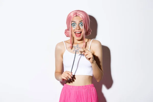 Portret atrakcyjnej dziewczyny z różową peruką i jasnym makijażem, przebrany za wróżkę na halloween party, trzymając magiczną różdżkę i uśmiechając się — Zdjęcie stockowe