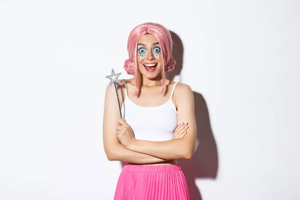 Porträtt av attraktiv flicka med rosa peruk och ljus makeup, utklädd till en älva för halloween fest, håller magiska trollspö och leende — Stockfoto