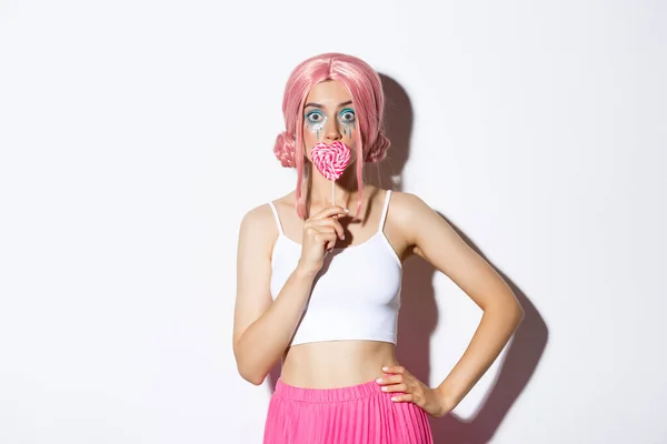Piękna uśmiechnięta dziewczyna w różowej peruce, trzymając cukierki w kształcie serca, trick lub psikus w stroju bajki na halloween, stojąc nad białym tle — Zdjęcie stockowe