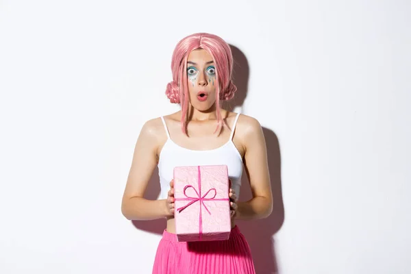 Retrato de chica atractiva sorprendida mirando emocionada, recibir regalo para el cumpleaños, usando peluca rosa, de pie sobre fondo blanco — Foto de Stock