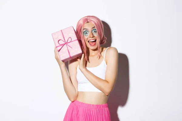 Porträtt av förvånad attraktiv flicka ser upphetsad, få present till födelsedag, bär rosa peruk, står över vit bakgrund — Stockfoto