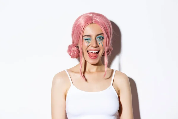 Närbild av ganska coquettish flicka i rosa peruk, blinkar vid kameran och ler, står över vit bakgrund — Stockfoto
