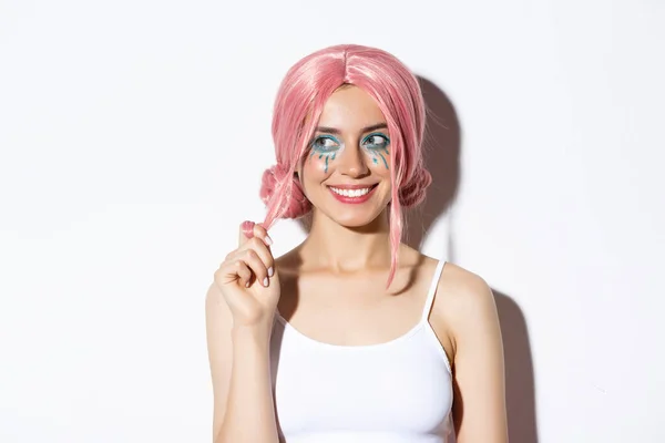 Närbild av coquettish leende flicka i rosa peruk, ser vänster fascinerad, står över vit bakgrund — Stockfoto
