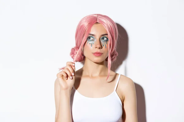 Närbild av omtänksam attraktiv flicka med rosa anime peruk och ljus makeup, tittar på övre vänstra hörnet banner och tänkande, gör val, står över vit bakgrund — Stockfoto