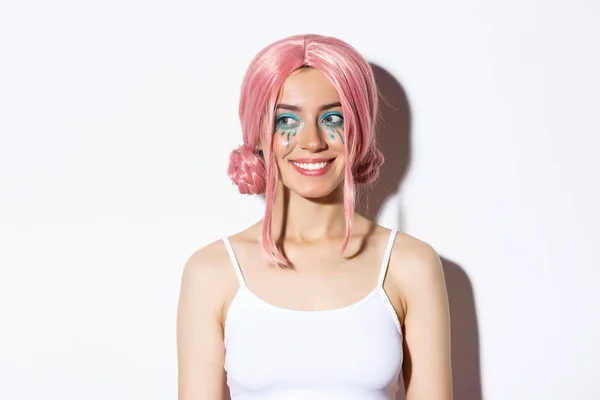 Närbild av vackra kaukasiska flicka i rosa peruk, med ljusa makeup, tittar vänster på logotyp och leende, står över vit bakgrund — Stockfoto