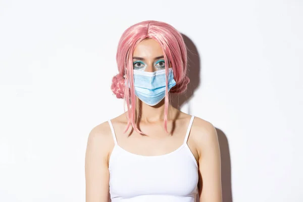 Крупним планом дівчина в рожевій перуці і медичній масці, святкування Хеллоуїна під час пандемії коронавірусу, стоїть на білому тлі — стокове фото