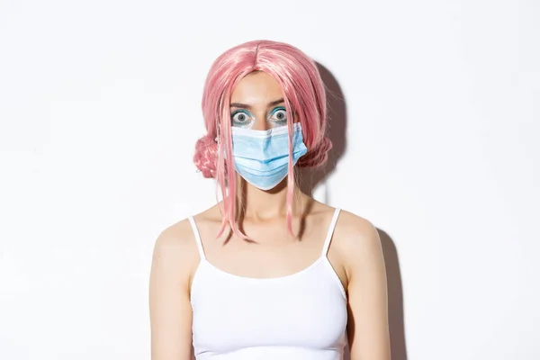 Крупним планом здивована дівчина в рожевій перуці і медична маска, дивлячись на камеру здивована, захищає себе від коронавірусної хвороби, стоїть на білому тлі — стокове фото