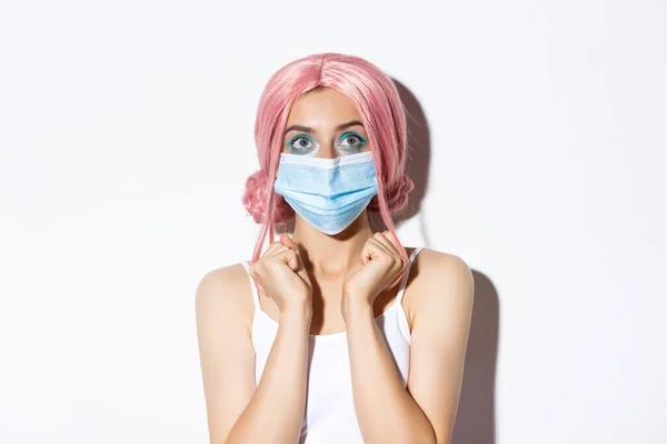 Концепція Covid-19. Крупним планом сподіваюся мила дівчина в медичній масці, дивлячись вгору збуджений, стоїть над білим тлом в рожевій перуці — стокове фото