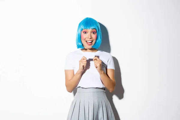 Podekscytowana ładna azjatycka dziewczyna pokazuje kartę kredytową, nosi niebieską perukę na halloween party, stoi na białym tle — Zdjęcie stockowe