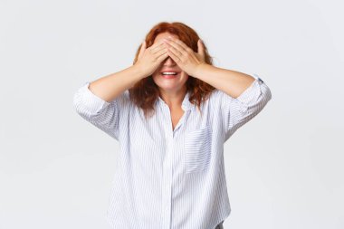 Şaşırmış ve eğlenmiş, orta yaşlı, mutlu, çocukları bekleyen kızıl saçlı kadın sürprizler getiriyor, çocuklarla oynayan genç büyükanne saklambaç oynuyor, ellerle gözlerini örtüyor, gülümsüyor ve gözleri bağlı duruyor.