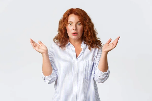 Astonished and concerned middle-aged redhead woman, mother react to confusing strange news, raise hands sideways and gasping worried, standing white background — Stock Photo, Image