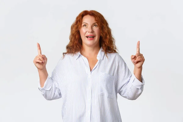 Wondered and amazed, upbeat middle-aged woman react to wonderful news, pointing and looking up with excited smile, reading banner, react to awesome promo offer, standing white background — Stock Photo, Image