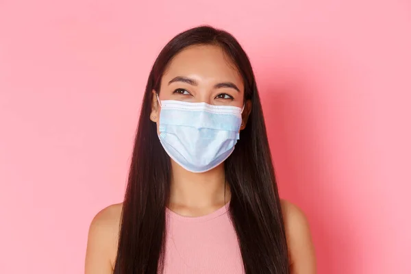 Covid-19 pandemi, coronavirus och social distansering koncept. Närbild av bekymmersfri, glad attraktiv asiatisk flicka i medicinsk mask skrattar medan du tittar övre vänstra hörnet, rosa bakgrund — Stockfoto