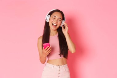 Çekici stil sahibi Asyalı kızın belden yukarı portresi. Gözlerini kapat ve kulaklıkla müzik dinlerken şarkı söyle. Cep telefonuyla karaoke oyunu oyna.