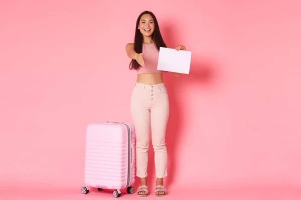 Viaggiare, vacanze e concetto di vacanza. Full-length di amichevole sorridente ragazza asiatica turista in piedi vicino a valigia con segno di carta e allungare la mano per stretta di mano, incontro in aeroporto — Foto Stock