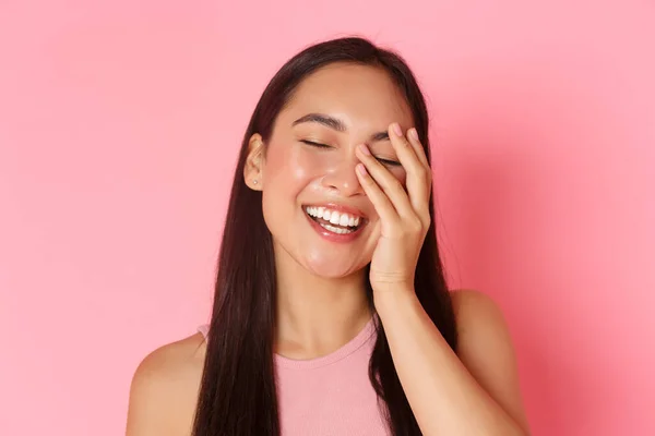 Beauté, mode et style de vie concept. Gros plan de belle jeune fille asiatique sans acné ni imperfections, sourire blanc, toucher le visage et regarder heureux, debout sur fond rose — Photo