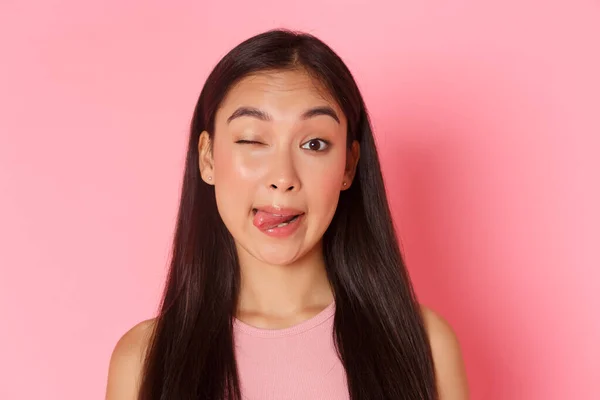 Conceito de beleza, moda e estilo de vida. Close-up de bonito e bobo, kawaii menina asiática fazendo caras engraçadas, mostrando a língua e piscar na câmera atrevida, de pé sobre o fundo rosa — Fotografia de Stock