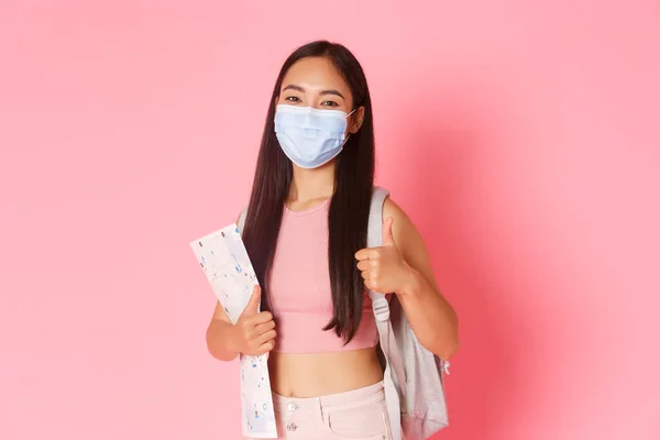 Safe tourism, travelling during coronavirus pandemic and preventing virus concept. Cheerful cute asian girl tourist encourage social distance while travel abroad, show thumbs-up and wear medical mask — Stock Photo, Image