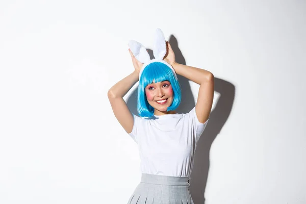 穿着蓝色短假发和兔耳的可爱的笑脸亚洲女孩的画像，看着相机傻傻的，穿着派对服装，站在白色背景上 — 图库照片