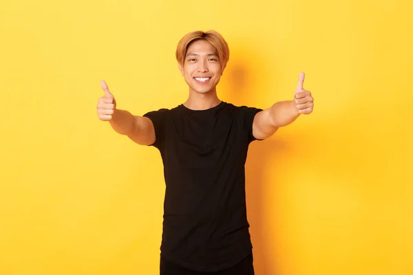 Портрет запевненого красивого азіатського чоловіка, що показує великі пальці в схваленні, як ідея, що стоїть на жовтому тлі — стокове фото