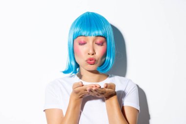 Parlak makyajlı, mavi peruklu, hava öpücüğü veren cadılar bayramı kostümü giymiş aptal Asyalı kadının yakın çekimi.