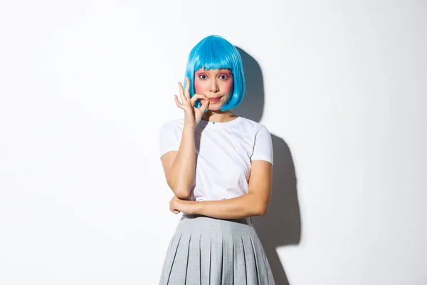 Portret coquettish azjatyckiej dziewczyny w niebieskiej peruce uszczelnić usta i obiecać, że nie zdradzić sekret, stojąc na białym tle — Zdjęcie stockowe