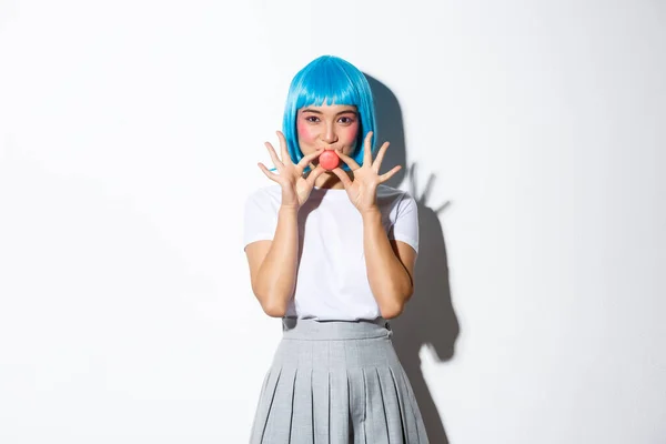 Coquettish azjatycki dziewczyna w niebieski peruka pokazując makaron w pobliżu usta i uśmiechnięty, stojąc na białym tle — Zdjęcie stockowe