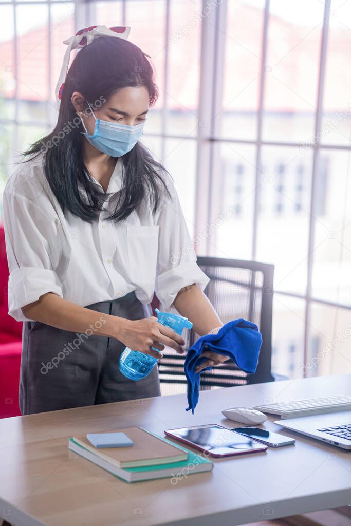 young asian woman cleaning her computer desk and equipment to protect covid19 virus infection